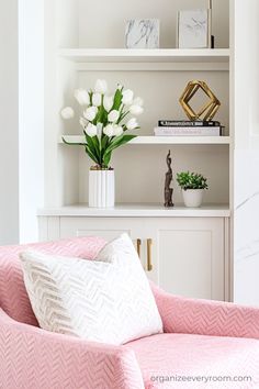 a pink chair in front of a white book shelf with flowers on it and some books