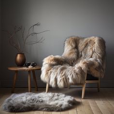 a chair with fur on it next to a small table and plant in the corner