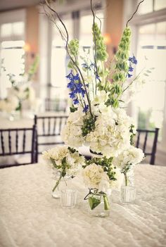 a vase filled with white and blue flowers on top of a round table covered in chairs