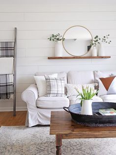 a living room with white couches and pillows on top of the coffee table in front of a round mirror