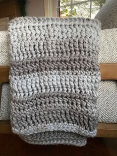 a gray and white knitted blanket sitting on top of a wooden bench next to a window