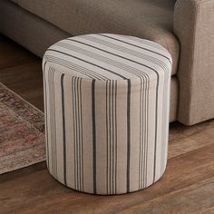 a striped ottoman sitting on top of a wooden floor next to a couch and rug