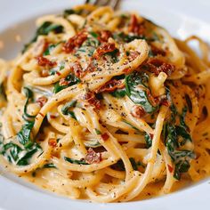 a white plate topped with pasta and spinach covered in cheese, sauce and seasoning