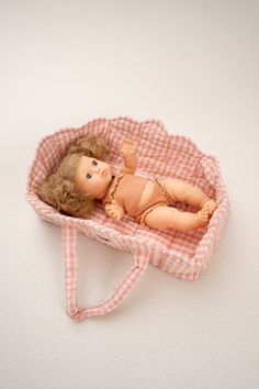 a doll is laying in a pink and white checkered cloth bag on a white surface