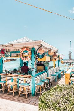 a man sitting at a bar in front of the ocean on a pier with chairs around it