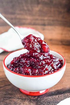 a spoon full of cranberry sauce in a red and white bowl on a wooden table