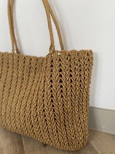 a crocheted bag hanging on the wall next to a white wall and wooden floor