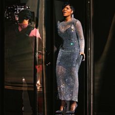 a woman standing in front of a mirror with a camera on her shoulder and wearing a silver dress