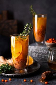 two glasses filled with drinks sitting on top of a table next to nuts and herbs