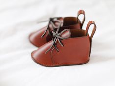 A symbol of enduring love and tenderness, these hand crafted leather baby shoes are designed to be cherished for generations. Classic lace up design, complete with leather laces and soles. Entirely made by hand, using traditional leather crafting methods for superior craftsmanship, attention to detail, and durability. Saddle stitched with wax linen thread. Hand painted edges with edge paint from France. Italian vegetable tanned leather is supple with good structure and a soft sheen. It will pati Lace-up Leather Shoes With Soft Sole, Leather Booties With Soft Sole For Gift, Gift Leather Booties With Soft Sole, Leather Booties With Soft Sole As Gift, Leather Moccasins With Soft Sole As Gift, Brown Lace-up Booties With Rubber Sole, Leather Mouse, Leather Mouse Pad, Linen Thread