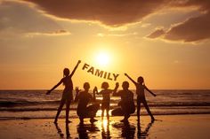 four people standing on the beach with their arms in the air and one person holding up a sign that says family