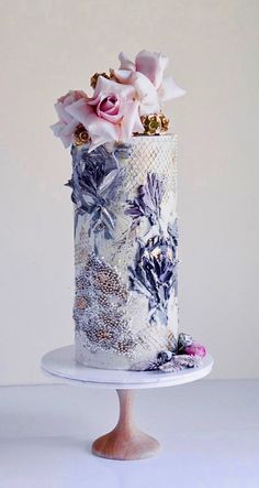 a three tiered cake decorated with flowers on a white tablecloth covered pedestal, against a plain background