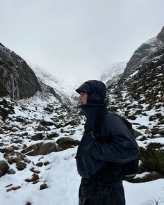 a man standing on top of a snow covered ground next to a mountain side with lots of rocks