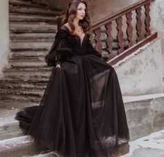 a woman in a long black dress standing on some steps