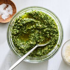 a glass bowl filled with pesto next to two wooden spoons on a white table