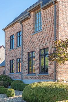 a large brick house with lots of windows and bushes in the front yard, surrounded by stone walkways