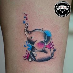 an elephant tattoo on the leg of a woman's thigh, with blue and pink paint splatters all over it