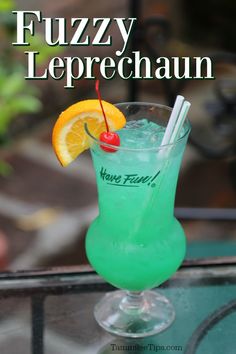 a green drink with orange and straw garnish on the rim sitting on a glass table