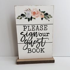 a sign that says please sign your guest book with flowers and leaves on the front