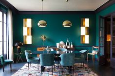 a dining room with green walls and blue upholstered chairs in front of the table