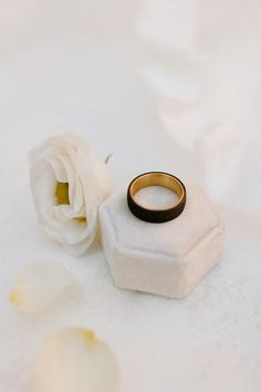 a white rose sitting next to a black and gold ring