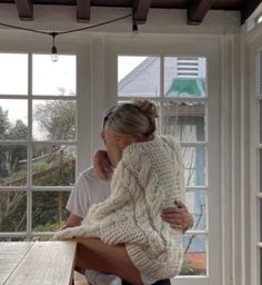 a man and woman sitting at a table in front of a window with their arms around each other