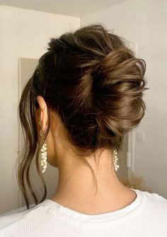 a woman with her hair in a low bun, wearing earrings and a white t - shirt