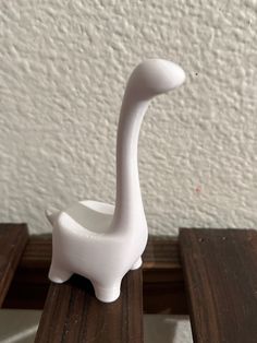 a small white ceramic bird sitting on top of a wooden table next to a wall