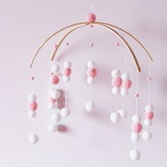 a pink and white mobile hanging from a wooden stick on a wall with balls attached to it