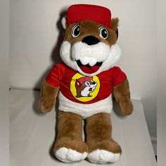 a brown and white stuffed bear wearing a red shirt with a cartoon character on it's chest