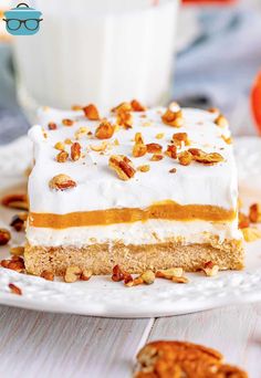 a piece of cake with white frosting and pecans on top sitting on a plate next to a glass of milk