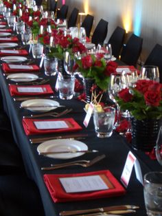 a long table is set with place settings and red flowers in vases on the tables