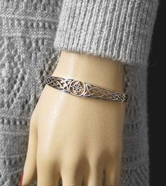 Material: 100% Sterling silver Weight: 11.0 grams Size: Front (widest part) of bracelet is almost 1/2 inch (12 mm) Inside measurements: Almost 2-1/2 inches x 2 inches (63 x 51 mm) Item number: wh086 This handsome cuff bracelet features a cut-out witch's knot, framed in a round border, front and center with an adjoining cut-out band to either side. It has a nice weight and thickness to it. Each side band is decorated with a simple woven Celtic knot pattern that repeats itself many times from fron Silver Metal Bangle Wristband, Silver Metal Bangle, Engraved Silver Bracelet Wristband, Engraved Silver Wristband, Adjustable Engraved Bangle, Elegant Silver Metal Wristband, Classic Silver Metal Bangle, Symbolic Nickel-free Silver Bracelets, Silver Cuff Jubilee Bracelet