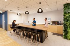 two people sitting at a counter in an office setting with bar stools and coffee machines