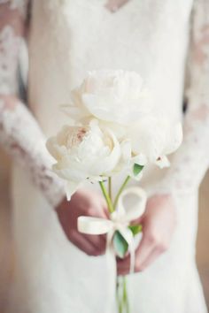 a woman holding a bouquet of white flowers in her hands and wearing a wedding dress