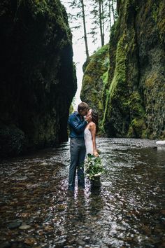 a bride and groom standing in the middle of a river surrounded by mossy cliffs