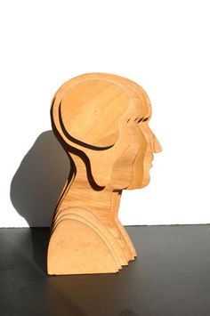 a wooden sculpture of a person's head on a black surface with a white wall in the background