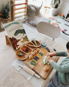 a young boy is playing with dinosaurs on a wooden table in front of a children's book