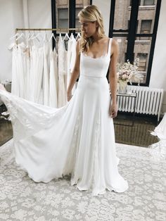 a woman standing in front of a rack of wedding dresses