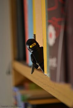 a lego man is peeking out from behind a book shelf with books in the background