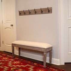 a bench sitting on top of a red rug in front of a white wall with hooks