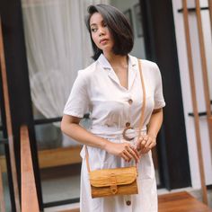 a woman in a white dress is holding a brown purse and looking off to the side