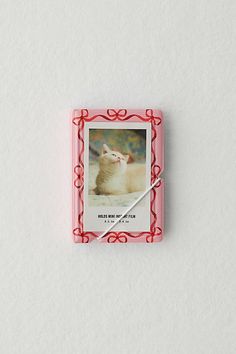 a small square photo frame with a white cat on it's front and red trim around the edges