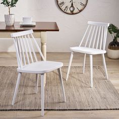 two white chairs sitting on top of a rug next to a table with a clock