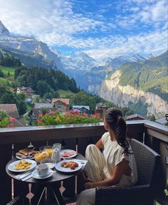 a woman sitting at a table with plates of food in front of her on a balcony