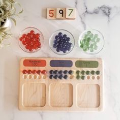 an assortment of beads and numbers on a wooden tray next to two bowls with flowers