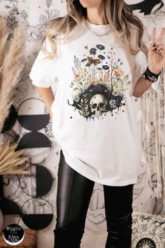 This whimsigoth fashion shirt is perfect for anyone who loves dark cottagecore, goblincore and whimsigoth aesthetics! It features a unique watercolor painting of a skull amongst flowers and butterflies. The perfect combination of whimsical gothic and cozy cottagecore, this tee will have you standing out in any crowd. Show off your fandom with this one-of-a-kind whimsigoth shirt. Whether you're attending a festival, meeting up with friends, or just want to add some color to your wardrobe, this sh Gothic Skull Print T-shirt For Fall, Cotton Skull Print Shirt For Fall, Fall Skull Print Cotton Shirt, Fall Cotton Shirt With Skull Print, Gothic Cotton Shirt For Alternative Fashion, Gothic Cotton T-shirt For Fall, Goblincore Cotton Streetwear Tops, Fairy Grunge Halloween Festival Tops, Cotton Shirt For Alternative Fashion In Fall