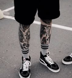 a person with tattoos standing in a parking lot wearing black and white tennis shoes on their feet