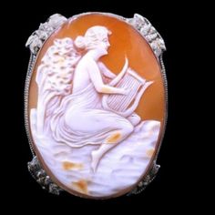 This Stunning Antique Edwardian Carved Shell Cameo Is Set In Beautifully Detailed 14k White Gold. A Large Piece, It Shows Euterpe, The Greek Muse Of Music, Playing Her Lyre. She Is Classically Attired In Flowing Robes. The Carving Is Very Detailed And In Excellent Condition. The 14k White Gold Setting Perfectly Enhances The Piece. Flowers And Leaves Accent Each Side. The Brooch Also Has A Flip Up Bale To Wear As A Pendant. The Only Blemish Is A Small Chip Below The Bale. 1 3/4 By 1 1/4". Exquisite White Brooch For Formal Occasions, White Cameo Brooch For Formal Occasions, White Cameo Brooches For Formal Occasion, White Oval Brooch For Formal Occasions, Antique White Brooch For Formal Occasions, White Art Deco Brooches For Formal Occasions, Antique White Formal Brooch, White Oval Cameo Brooches, White Oval Brooch For Anniversary