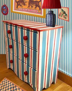 a blue and red striped chest with two lamps on it's sides next to a painting